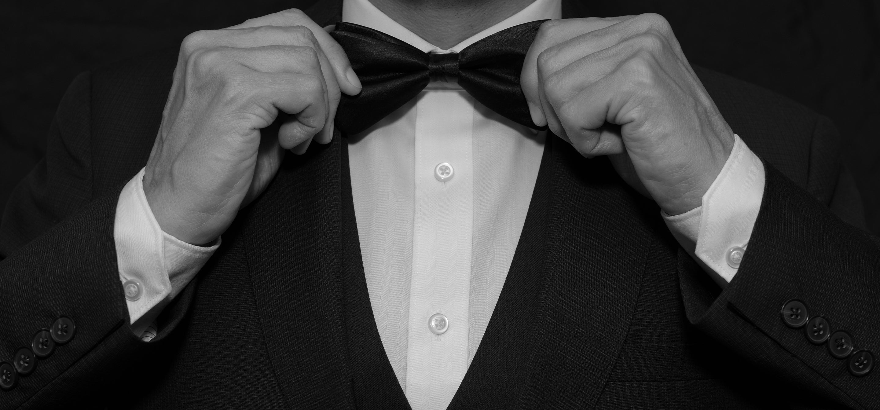 Man in a dark suit adjusting his bow tie